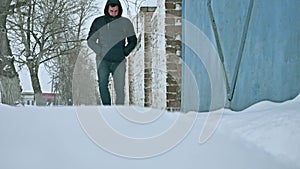 Man walks in the winter through the snow city of an old brick fence. poor man walks in the snow in outdoors winter