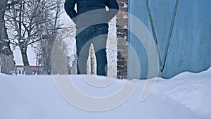 Man walks in the winter through the snow city of an old brick fence. poor man walks in the snow in winter outdoors