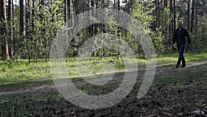 A man walks through the woods drinking a drink and throwing out a plastic bottle, litter