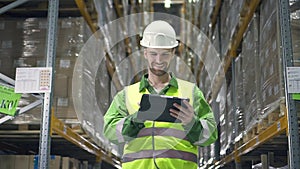 man warehouse worker in storage rack with merchandise looks at digital tablet and smiles. male