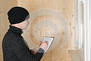 A man in warm clothes and a hat writes down the results of the work on warming the loggia