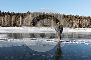 Man in warm clothes standing on the thin ice of a frozen river,