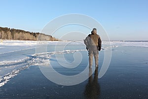 Man in warm clothes walking along the thin ice of a frozen river in the evening