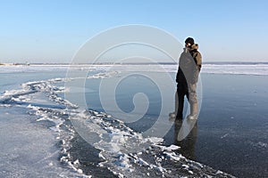 Man in warm clothes walking along the thin ice of a frozen river in the evening