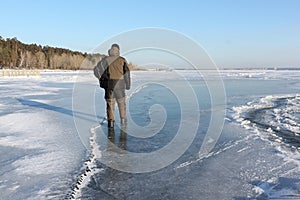 Man in warm clothes walking along the thin ice of a frozen river in the evening