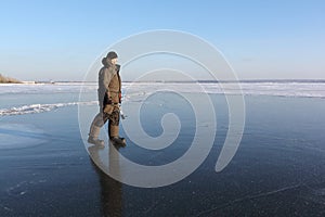 Man in warm clothes walking along the thin ice of a frozen river in the evening