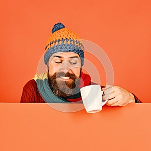 Man in warm hat holds white cup on orange background