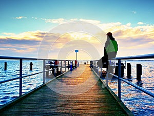 Man in warm jacket and baseball cap sit on pier and enjoy quiet morning sea. Tourist relax.