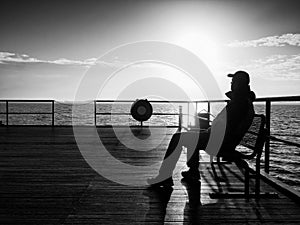 Man in warm jacket and baseball cap sit on pier and enjoy quiet morning sea. Tourist relax.