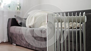 A man in a warm jacket with a hood lies on the sofa against the backdrop of a switched-on electric heater. The concept