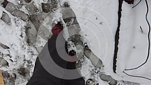 A man in warm pants and boots walks neatly along the sidewalk on which wet snow has frozen and formed ice