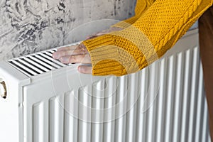 Man warming his hands in yellow sweater on the heater at home during cold winter days. Male getting warm up his arms