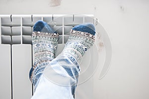 Man warming legs on heating radiator near white wall