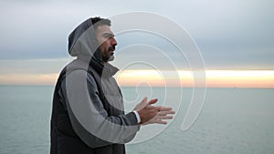 Man is warming up his hands by breathing at the cold morning seaside. Morning sunrise over the sea.