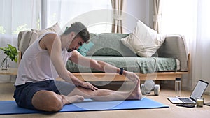 Man warming up, stretching legs and watching fitness video tutorial online on laptop.