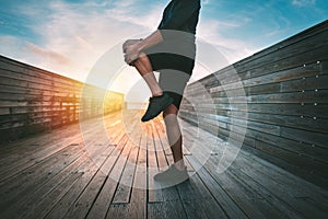 Man warming up and stretching legs before workout outdoors at sunset or sunrise