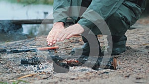 A man warms his hands over a fire on an autumn day near a pond.