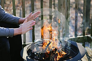 Man Warms His Hands Over a Fire Pit on a Deck.