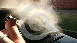 Man washes the car thoroughly. Wash using high pressure water jet. Sun shines
