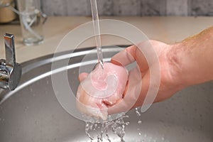 A man washes defrosted raw chicken fillet. Fresh raw chicken breast for cooking chopped chicken cutlets. A man washes