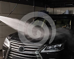 A man washes foam off a black car with water at a car wash.