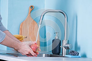 A man washes fruit in a sink in a kitchen with blue walls. Against the background of fruits