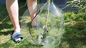 A man washes a glass twenty-liter bottle with a narrow neck with an electric drill, a stick and rags with water.