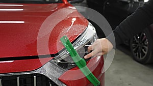 A man washes the headlights of a red car with a scraper.