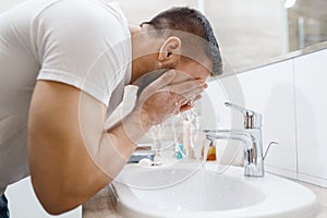 Man washes his face in bathroom, morning hygiene