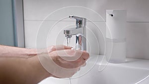 A man washes his hands in his bathroom. Men`s hands in the frame, a modern house with an automatic foam dispenser.