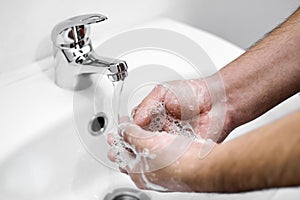 A man washes his hands with soap over a white sink as a prophylaxis against coronovirus infection COVID-19. Volumetric foam. Healt