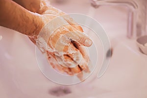 A man washes his hands with soap suds over a white ceramic sink in the bathtub. Cleanliness and hygiene