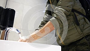 A man washes his hands using a touchless faucet in a restroom