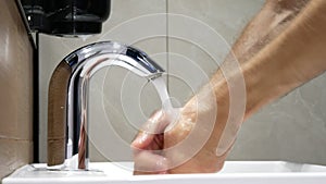A man washes his hands using a touchless faucet and a touchless soap dispenser