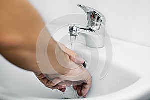 A man washes his hands with water over a white sink in the bathroom in daylight. Preventive measures against viral infection. Pers