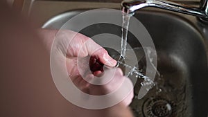 man washes a large knife under running water in a metal sink.Crime and murder symbol.