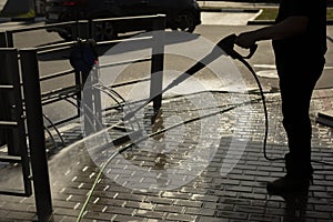 A man washes the paving tiles with a hose. Cleaning of the territory