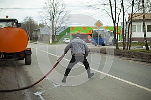 A man washes the road. Worker with a hose for water supply. Special city service in Russia. Cleaning of the territory