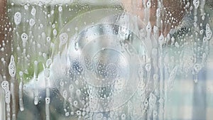 Man Washing and Cleaning a Window at Home using Cleanser Spray and Disinfectant Foam in Slow Motion. Household Chores.