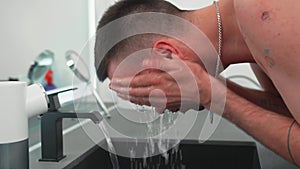 Man washing face rinsing in sink under running cold water from faucet, Morning skincare routine. Male beauty skin care