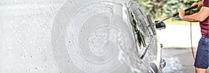 Man washing his car at self serve carwash, brush cleaning glass covered in shampoo. Left side is expanded to banner size, space