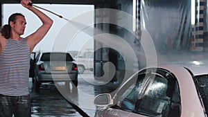 Man washing his car with water spray from high pressure washer. Car wash self-service. Caucasian man.