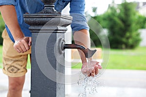 Man washing his hand in faucet water. Ð¡ity water tap with drinkable water in park. Drinking column.