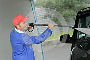 Man washing vehicle with pressurised hose