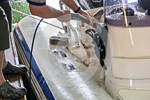 Man washing white inflatable boat with brush and pressure water system at garage. Ship service and seasonal maintenance concept