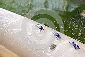 Man washing white inflatable boat with brush and pressure water system at garage. Ship service and seasonal maintenance concept