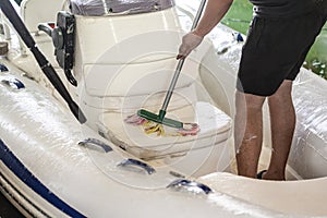 Man washing white inflatable boat with brush and pressure water system at garage. Ship service and seasonal maintenance concept