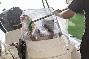 Man washing white inflatable boat with brush and pressure water system at garage. Ship service and seasonal maintenance concept