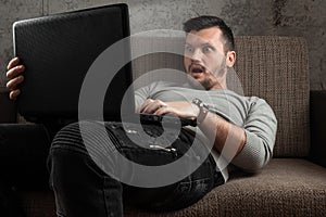 A man watches an adult video on a laptop while sitting on the couch. The concept of porn, masturbation, male needs, pervert, lust