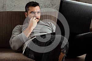 A man watches a video in a laptop while sitting on the couch is very surprised. Concept porn videos, admiration, desire